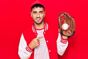 Wall Mural - Young hispanic man wearing baseball uniform holding golve and ball smiling happy pointing with hand and finger