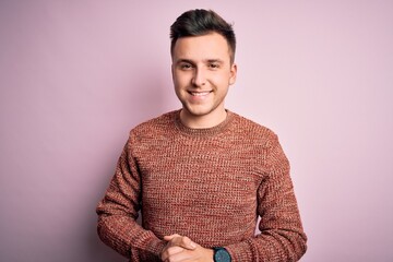 Wall Mural - Young handsome caucasian man wearing casual winter sweater over pink isolated background with hands together and crossed fingers smiling relaxed and cheerful. Success and optimistic