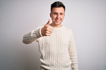 Wall Mural - Young handsome caucasian man wearing casual winter sweater over white isolated background doing happy thumbs up gesture with hand. Approving expression looking at the camera showing success.