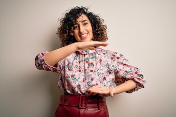 Sticker - Young beautiful curly arab woman wearing floral t-shirt standing over isolated white background gesturing with hands showing big and large size sign, measure symbol. Smiling looking at the camera