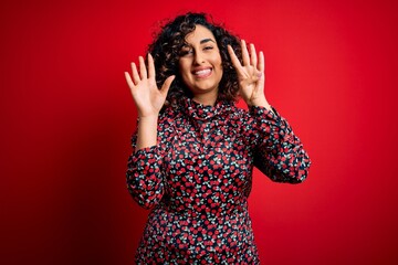 Sticker - Young beautiful curly arab woman wearing casual floral dress standing over red background showing and pointing up with fingers number nine while smiling confident and happy.