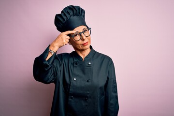 Sticker - Middle age brunette chef woman wearing cooker uniform and hat over isolated pink background pointing unhappy to pimple on forehead, ugly infection of blackhead. Acne and skin problem