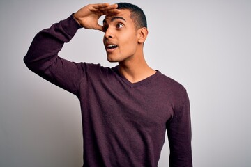 Wall Mural - Young handsome african american man wearing casual sweater over white background very happy and smiling looking far away with hand over head. Searching concept.