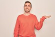 © Krakenimages.com - Young handsome man with blue eyes wearing casual sweater standing over white background smiling cheerful presenting and pointing with palm of hand looking at the camera.