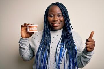 Sticker - African american plus size woman with braids holding plastic teeth over white background happy with big smile doing ok sign, thumb up with fingers, excellent sign