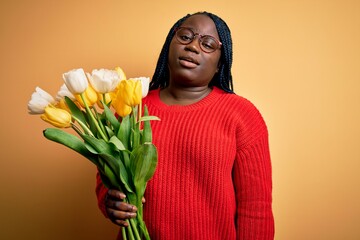 Sticker - Young african american plus size woman with braids holding bouquet of yellow tulips flower looking sleepy and tired, exhausted for fatigue and hangover, lazy eyes in the morning.