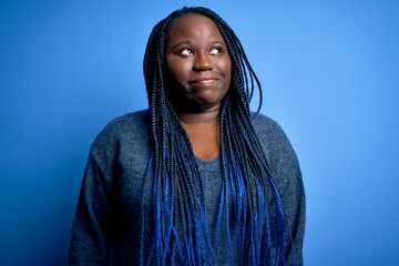 Poster - African american plus size woman with braids wearing casual sweater over blue background smiling looking to the side and staring away thinking.