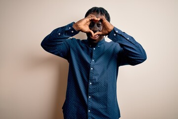 Sticker - Young handsome african american man wearing casual shirt standing over white background Doing heart shape with hand and fingers smiling looking through sign