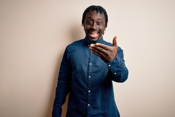 Wall Mural - Young handsome african american man wearing casual shirt standing over white background smiling friendly offering handshake as greeting and welcoming. Successful business.