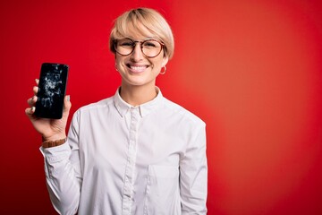 Poster - Young blonde woman with short hair holding broken smartphone over red background with a happy face standing and smiling with a confident smile showing teeth