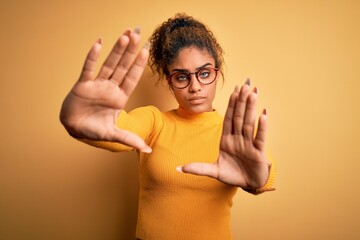 Poster - Young beautiful african american girl wearing sweater and glasses over yellow background doing frame using hands palms and fingers, camera perspective