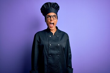 Sticker - Young african american chef girl wearing cooker uniform and hat over purple background angry and mad screaming frustrated and furious, shouting with anger. Rage and aggressive concept.