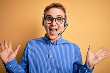 Wall Mural - Young handsome redhead call center agent man wearing glasses working using headset celebrating crazy and amazed for success with arms raised and open eyes screaming excited. Winner concept