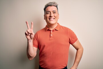 Young handsome modern man standing over isolated background smiling with happy face winking at the camera doing victory sign. Number two.