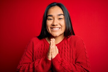 Poster - Young beautiful asian woman wearing casual sweater standing over isolated red background praying with hands together asking for forgiveness smiling confident.