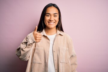 Poster - Young beautiful asian woman wearing casual shirt standing over pink background doing happy thumbs up gesture with hand. Approving expression looking at the camera showing success.