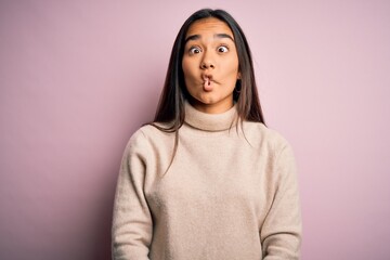 Poster - Young beautiful asian woman wearing casual turtleneck sweater over pink background making fish face with lips, crazy and comical gesture. Funny expression.