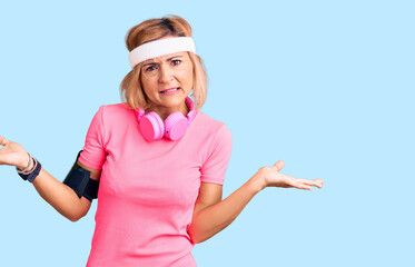 Poster - Young blonde woman wearing sportswear and headphones clueless and confused expression with arms and hands raised. doubt concept.