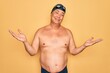 © Krakenimages.com - Middle age senior grey-haired swimmer man wearing swimsuit, cap and goggles clueless and confused expression with arms and hands raised. Doubt concept.