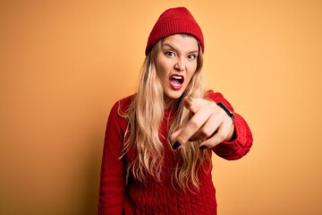 Poster - Young beautiful blonde woman wearing casual sweater and wool cap over white background pointing displeased and frustrated to the camera, angry and furious with you