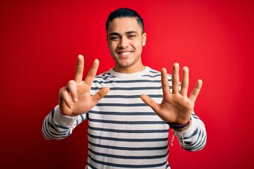 Wall Mural - Young brazilian man wearing casual striped t-shirt standing over isolated red background showing and pointing up with fingers number eight while smiling confident and happy.