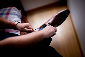 Sticker - Horizontal shot of a male tying his brown shoes sitting bed on a background of brown hardwood floor