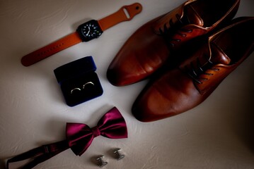 Poster - Top angle shot of brown male shoes, wedding rings, red bow, and a watch on a white surface