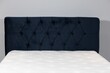 Closeup shot of a bed with dark blue fabric headboard and white mattress