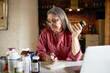 © shurkin_son - Portrait of middle aged female nutritionist in eyeglasses making research, sitting in front of open laptop, handwriting in copybook, studying dietary supplements, holding bottle of vitamins
