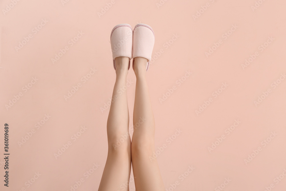 Female legs in soft slippers on color background