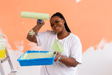 Pretty Smiling African American Woman Painting Interior Wall Of Home With Paint Roller. Redecoration, Renovation, Apartment Repair And Refreshment Concept.
