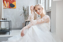Ideal Bride Sitting On The Floor, Portrait Of A Girl In A Long White Dress. Beautiful Hair And Clean, Soft Skin. Wedding Hairstyle Blonde
