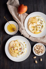 Ricotta with pears, pistachios and honey or maple syrup on two white plate on dark