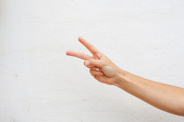 Hand with two fingers up in the peace, victory symbol or the letter V in sign language. Isolated on a white wall texture.