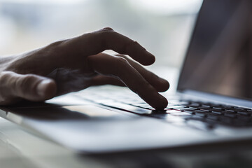 Businessman typing on laptop keyboard in sunny office, business and technology concept. Close up