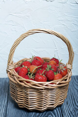 Ripe red strawberries in a wicker basket. Against the background of pine boards painted in white and black. Harvest 2020.