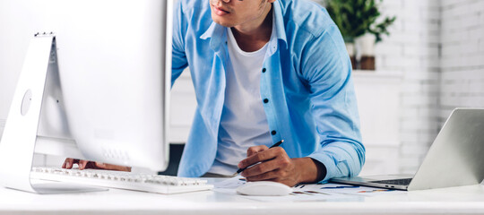 Young creative smiling happy asian man relaxing using desktop computer working and video conference meeting online chat at home.work from home concept