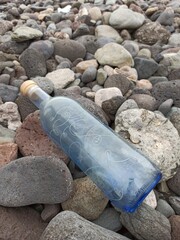 Sticker - Vertical closeup shot of a blue water bottle with a note inside on the rocks by the beach