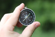 © yarbeer - Old classic navigation compass in hand on natural background as symbol of tourism with compass, travel with compass and outdoor activities with compass