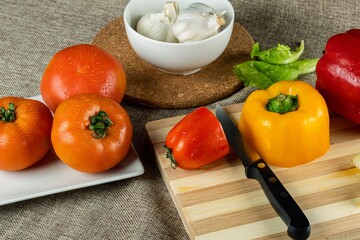 Wall Mural - Closeup shot of colorful peppers on a wooden cutting board tomatoes and garlic in the bowl