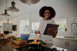 © StratfordProductions - Young african woman watching recipe in digital tablet while cooking lunch in modern kitchen