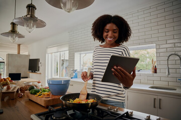 Young african woman watching recipe in digital tablet while cooking lunch in modern kitchen