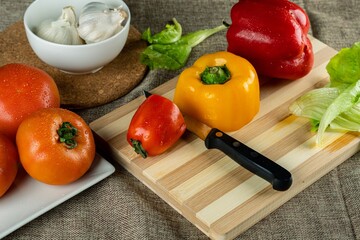 Wall Mural - Closeup shot of colorful peppers on a wooden cutting board tomatoes and garlic in the bowl