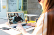 © Vadim Pastuh - Video call outdoors. A young woman sits in the summer cafe and uses laptop for video connection with a friend, coworker, she talks with an african-american guy