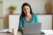 Woman In Headset Making Video Call Sitting At Laptop Indoor
