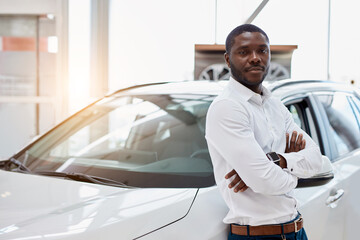 portrait of happy handsome african man in car dealership, afro man came to buy beautiful luxurious auto. successful purchase in cars showroom