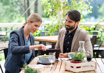 Happy couple sitting outdoors on terrace restaurant, eating.