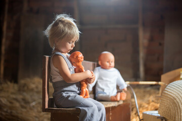 Poster - Little toddler boy, sitting on old vintage bench, holding doll  in attic