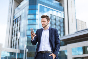 Confident young entrepreneur checking mobile phone for messages on city street