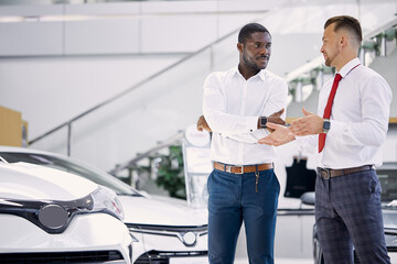 confident professional salesman talk about characteristics of car to customer man, black business man want to get necessary information about auto before making purchase, he asks questions